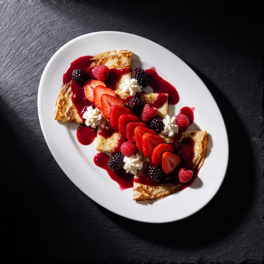 Crepes topped with strawberries, fresh fruit, whipped cream and fruit sauce.