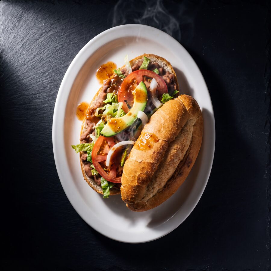 A Mexican torta on a telera roll filled with beans, lettuce, tomato and avocado.