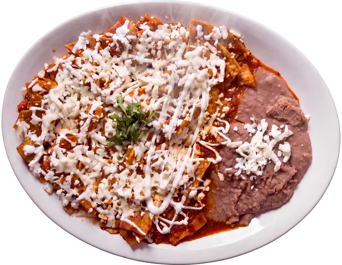 A plate of chilaquiles rojos seen from above: red salsa tortillas under shredded queso fresco and crema, with refried beans alongside.