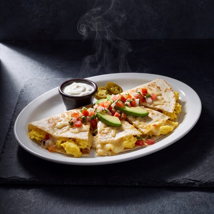 A breakfast quesadilla cut into wedges, seen from above on a white plate.